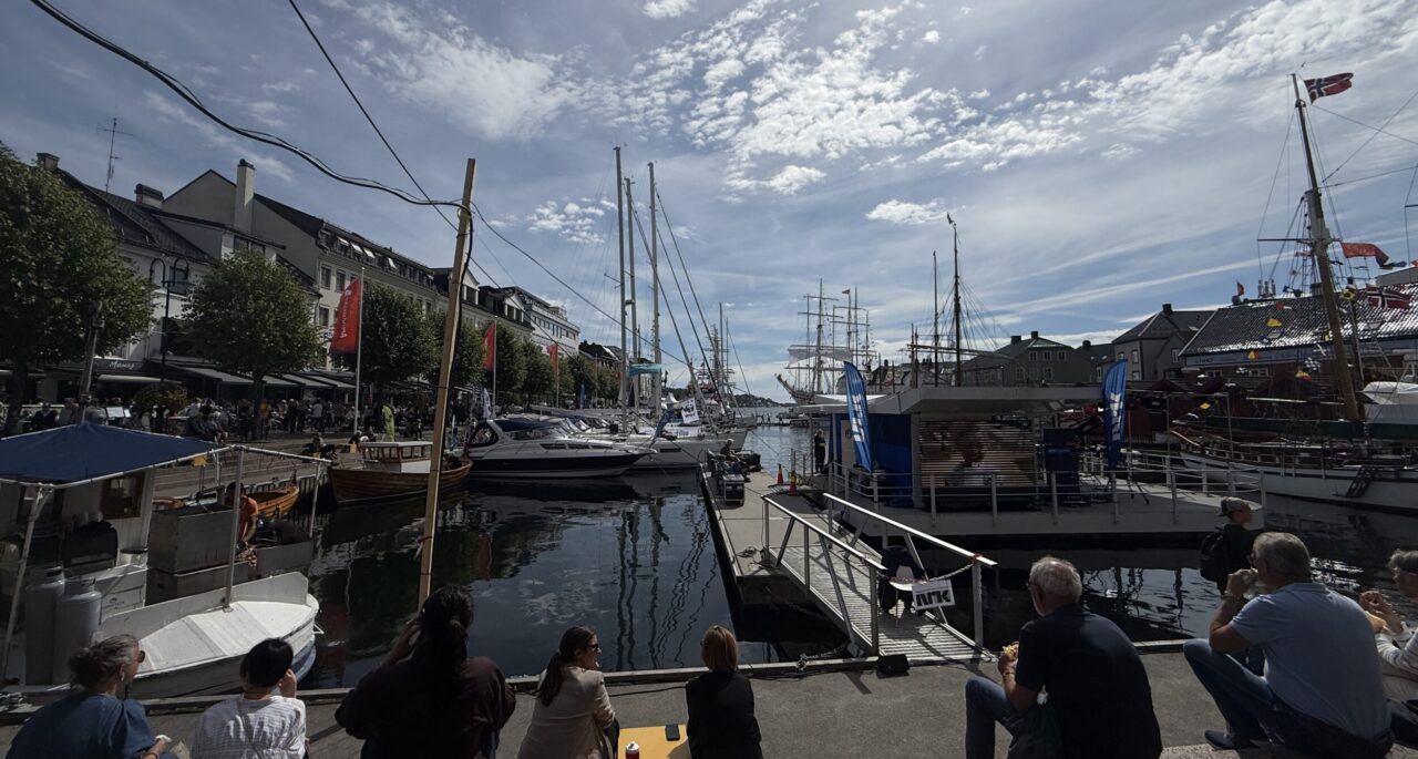 Arendalsuka. Pollen (havna) er full av båter, mennesker tar en pause på bryggekanten.