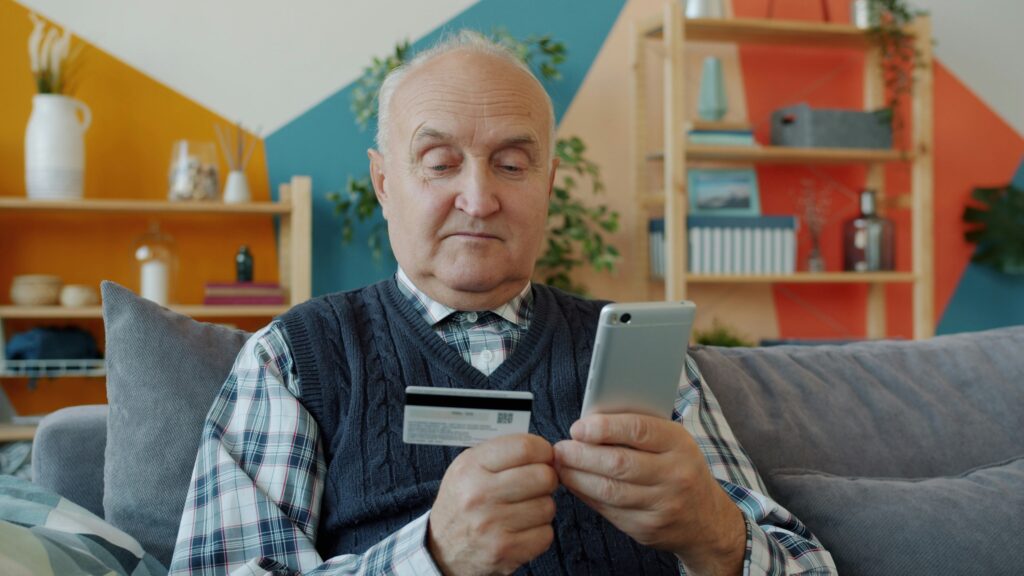 Eldre mann siotter med bankkort, og mobiltelefon.